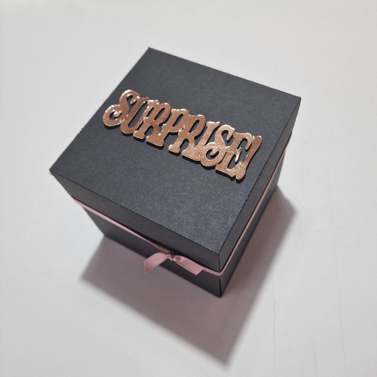 Exploding Occasions Box - Trip Reveal AMSTERDAM features a sleek black box with a pink ribbon, designed to unveil an Amsterdam-themed surprise with intricate landscape and verse panels inside.
