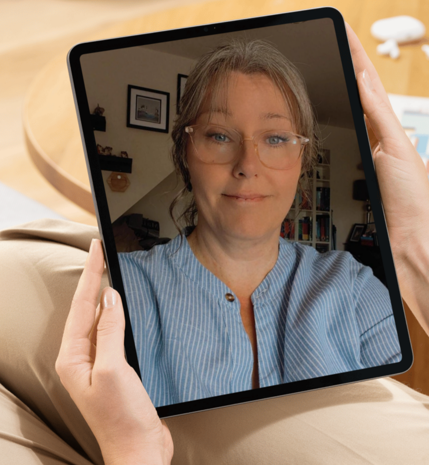 Person holding a tablet with a video call on screen, sitting on a couch.