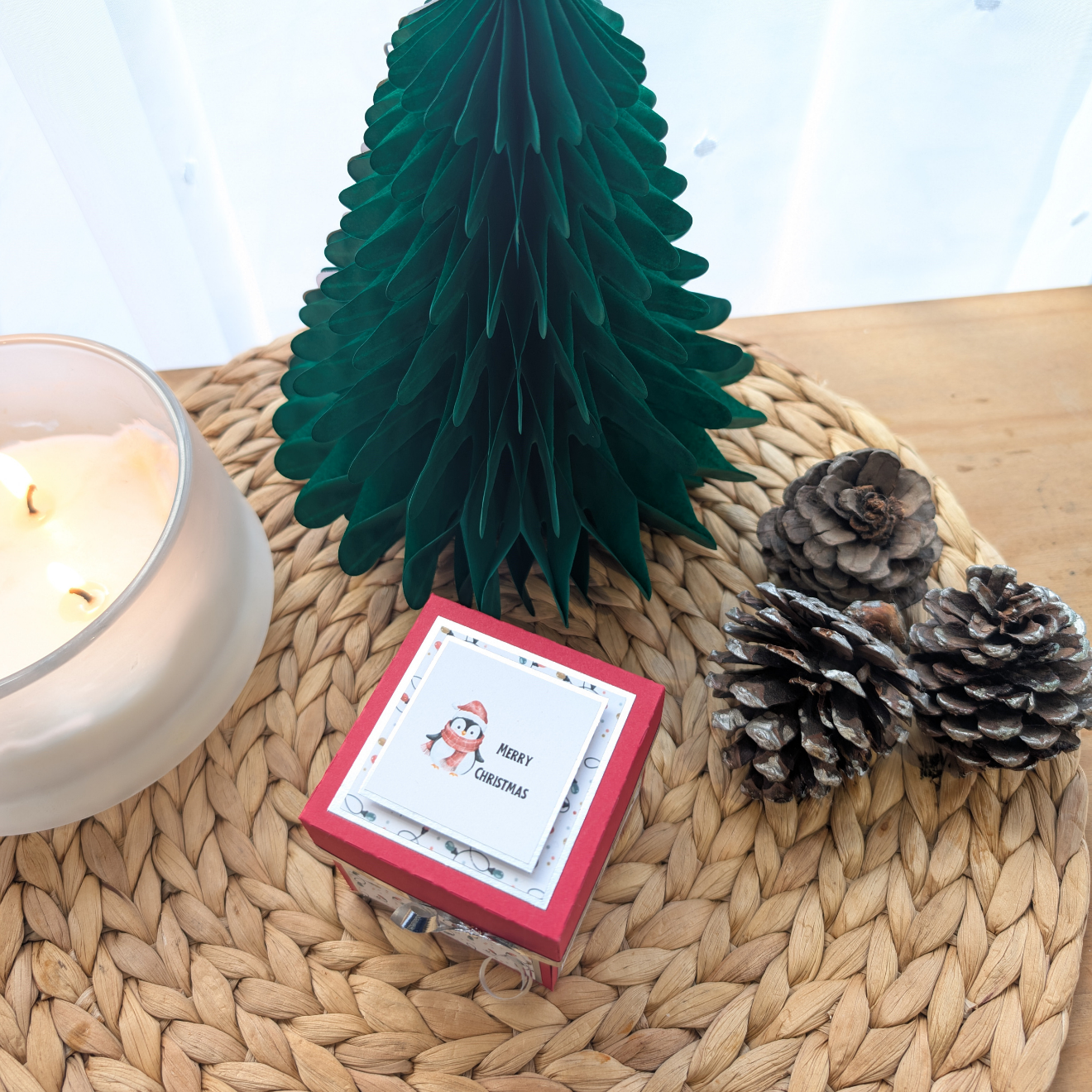 Frosty The Penguin Christmas Box Card displayed in a festive vignette with a three-wick candle, honeycomb tree, and pine cones, highlighting its charming pop-up design and penguin-themed greeting card.