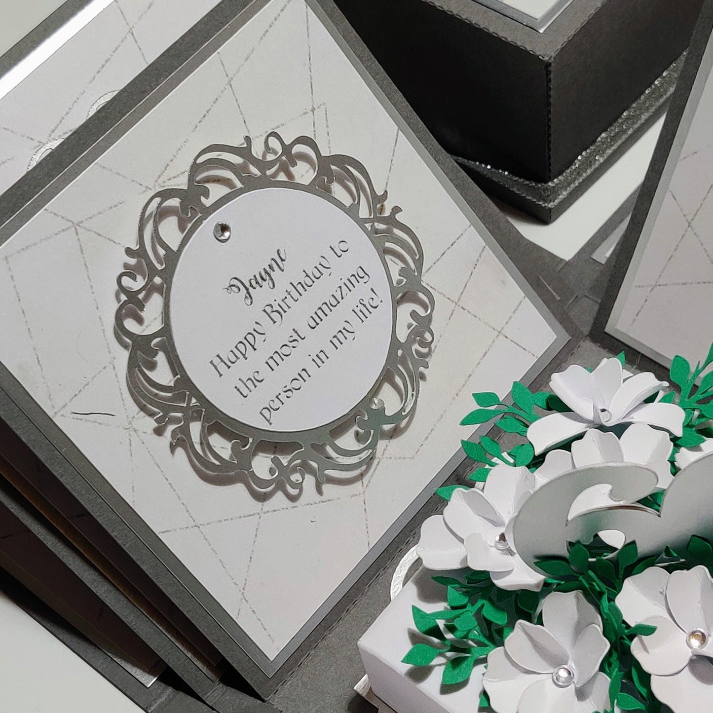 50th Birthday Celebration Occasion Box featuring a round card with black text, surrounded by flowers and foliage, elegantly packaged with birthday messages and a centerpiece highlighting the recipient's age.