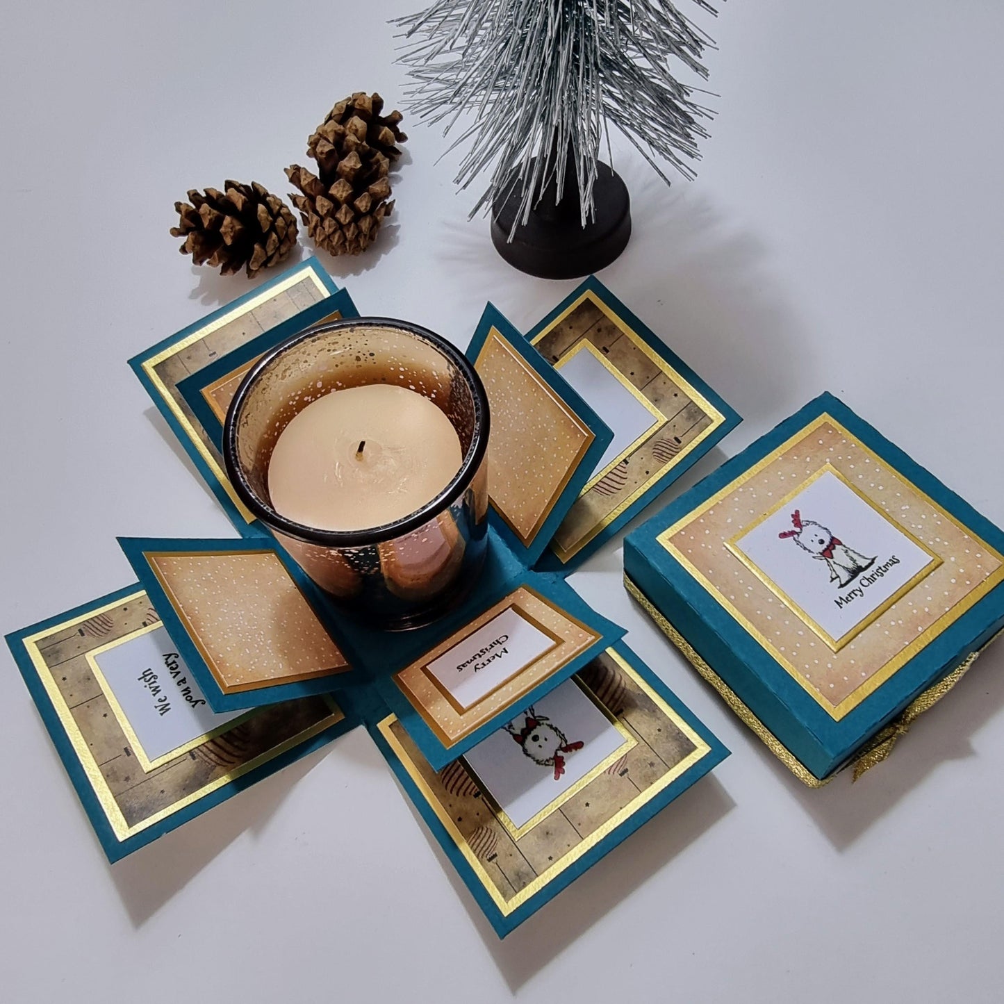 Lou Lou The Westie Christmas Candle Box featuring a festive-scented candle in a glass holder, placed on a teal green box adorned with a cheerful West Highland Terrier design.