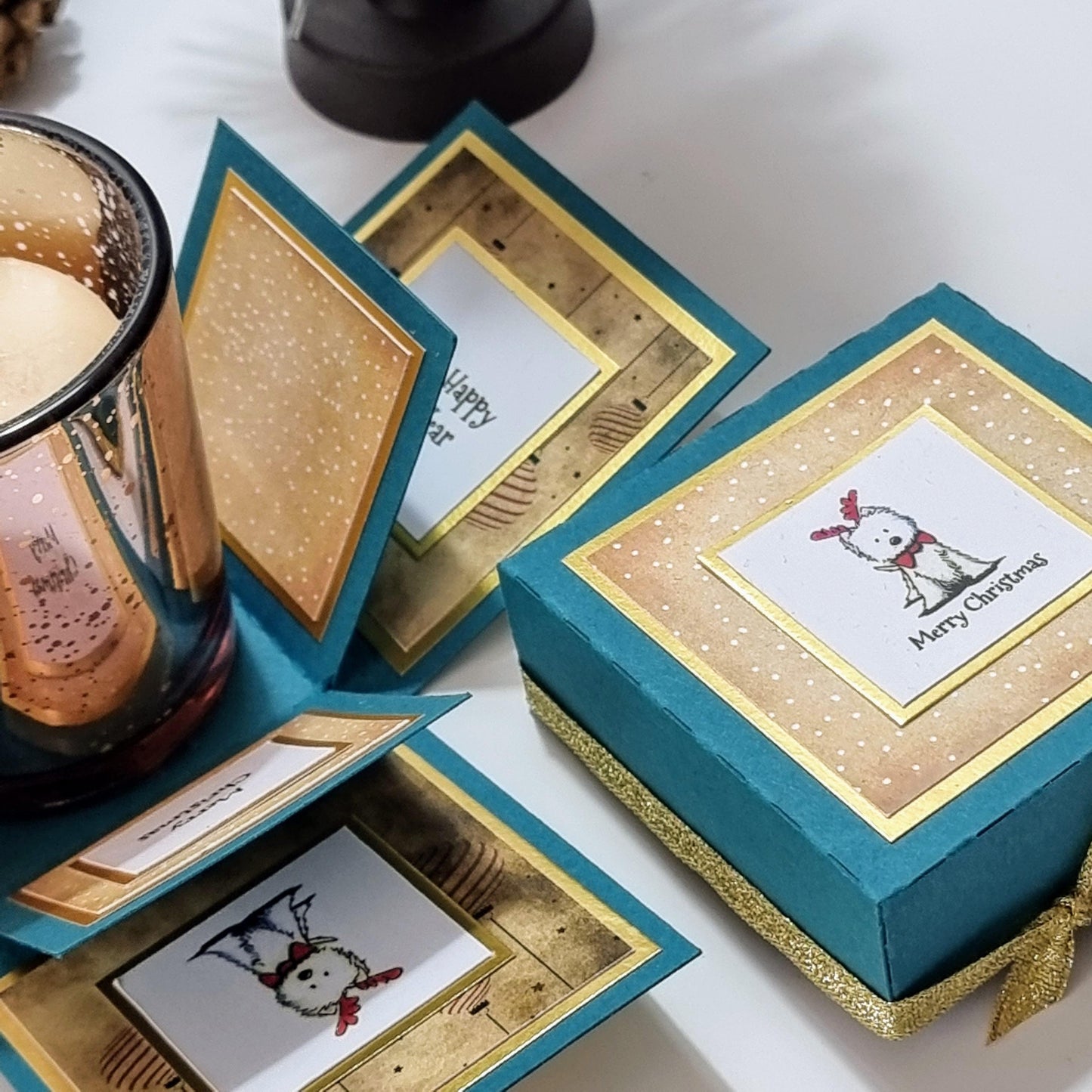 Lou Lou The Westie Christmas Candle Box features a teal box with gold accents, displaying a West Highland Terrier in Christmas attire and includes a votive candleholder with a festive scented candle.