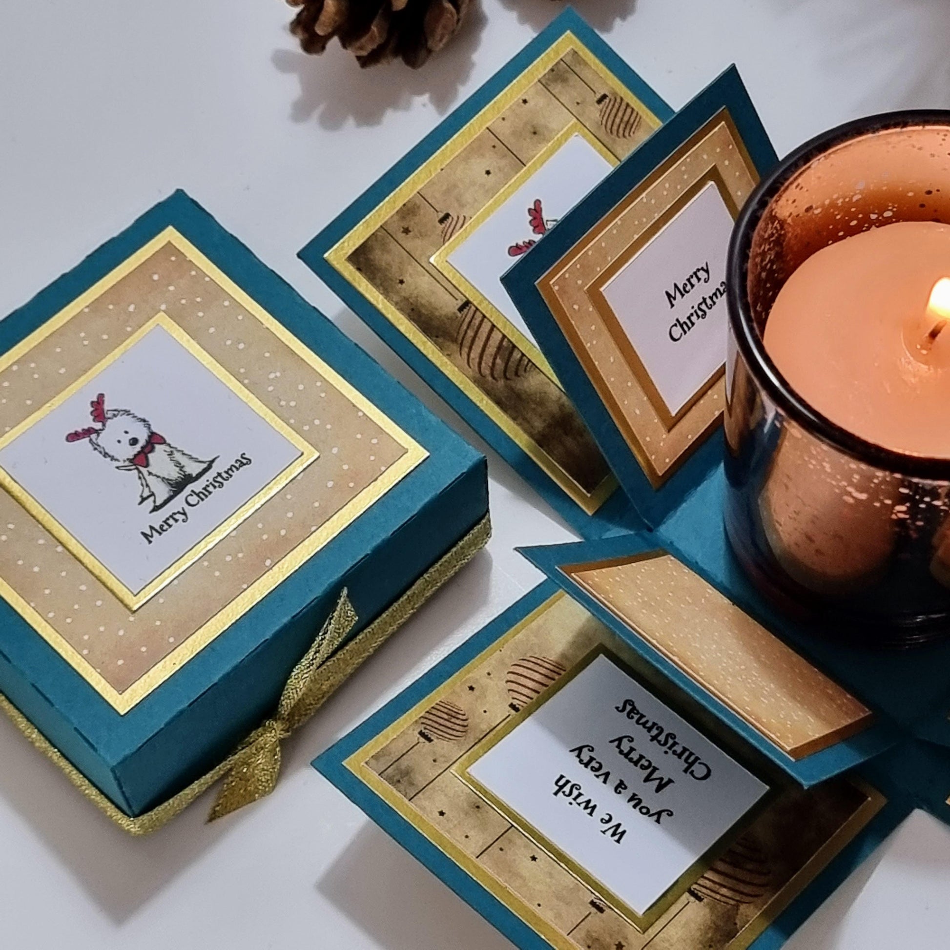 Lou Lou The Westie Christmas Candle Box features a teal green gift box with gold accents, containing a scented candle and a card with a West Highland Terrier in festive attire.