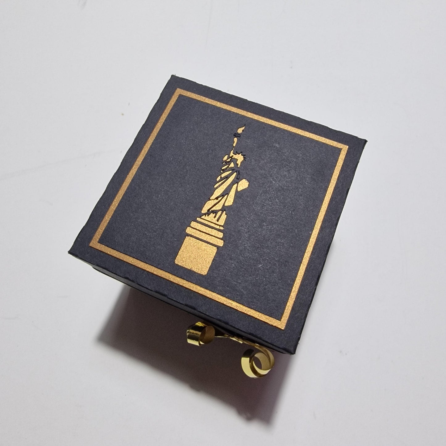 Exploding Occasions Box - Trip Reveal NEW YORK features a black box with intricate gold designs, highlighting a freestanding Statue of Liberty centerpiece, symbolizing the New York-themed surprise trip experience.