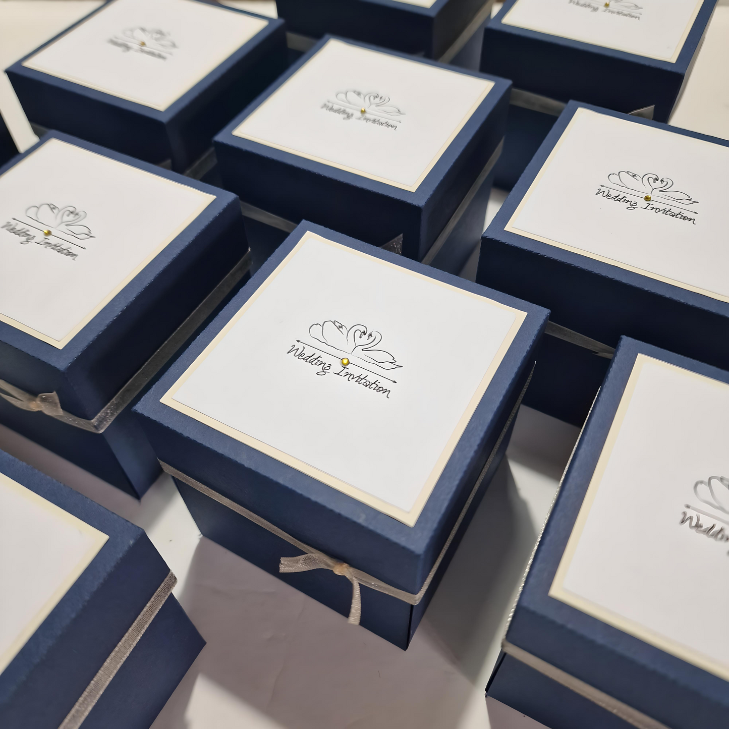 Swans Pocket Exploding Wedding Invitation Boxes featuring blue boxes with white labels and swan illustrations, centered around a three-tier heart-shaped cake adorned with doves.