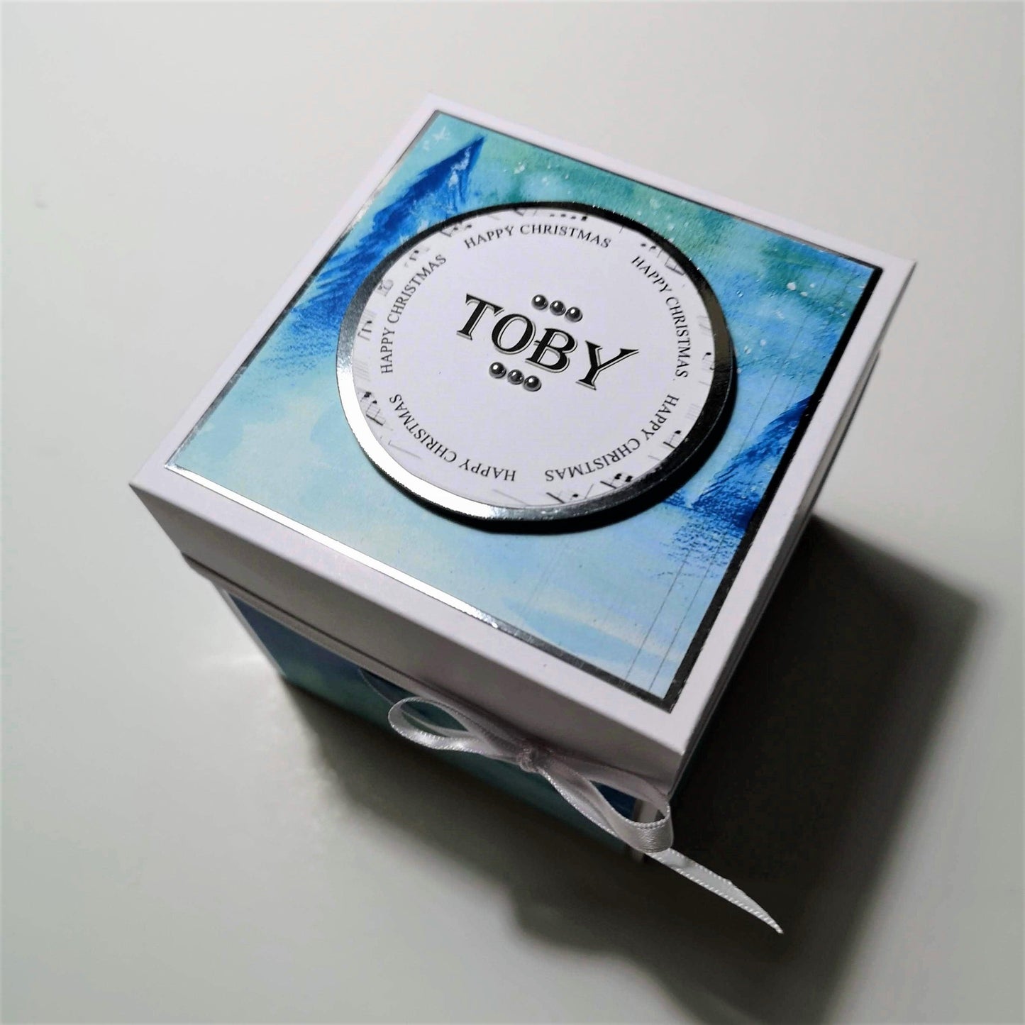 The Snowman Story Box features a blue and white box with a white ribbon, topped with a circular snowman statue, personalized with a name on the lid.