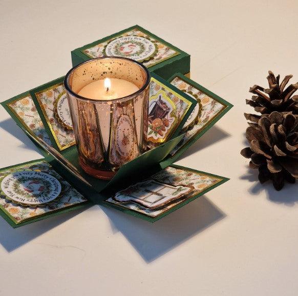 Vintage styled Christmas Candle Box featuring a votive candle in a glass holder, nestled alongside a pine cone, elegantly presented in a charming green box with festive embellishments.