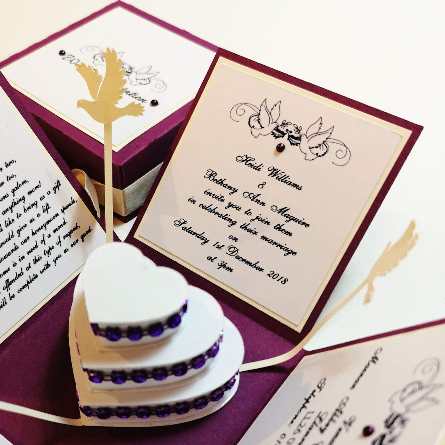 Purple & Cream Exploding Wedding Invitation Box featuring heart-shaped design with purple gems, a three-tier heart cake with doves, and panels for invitation and venue details.