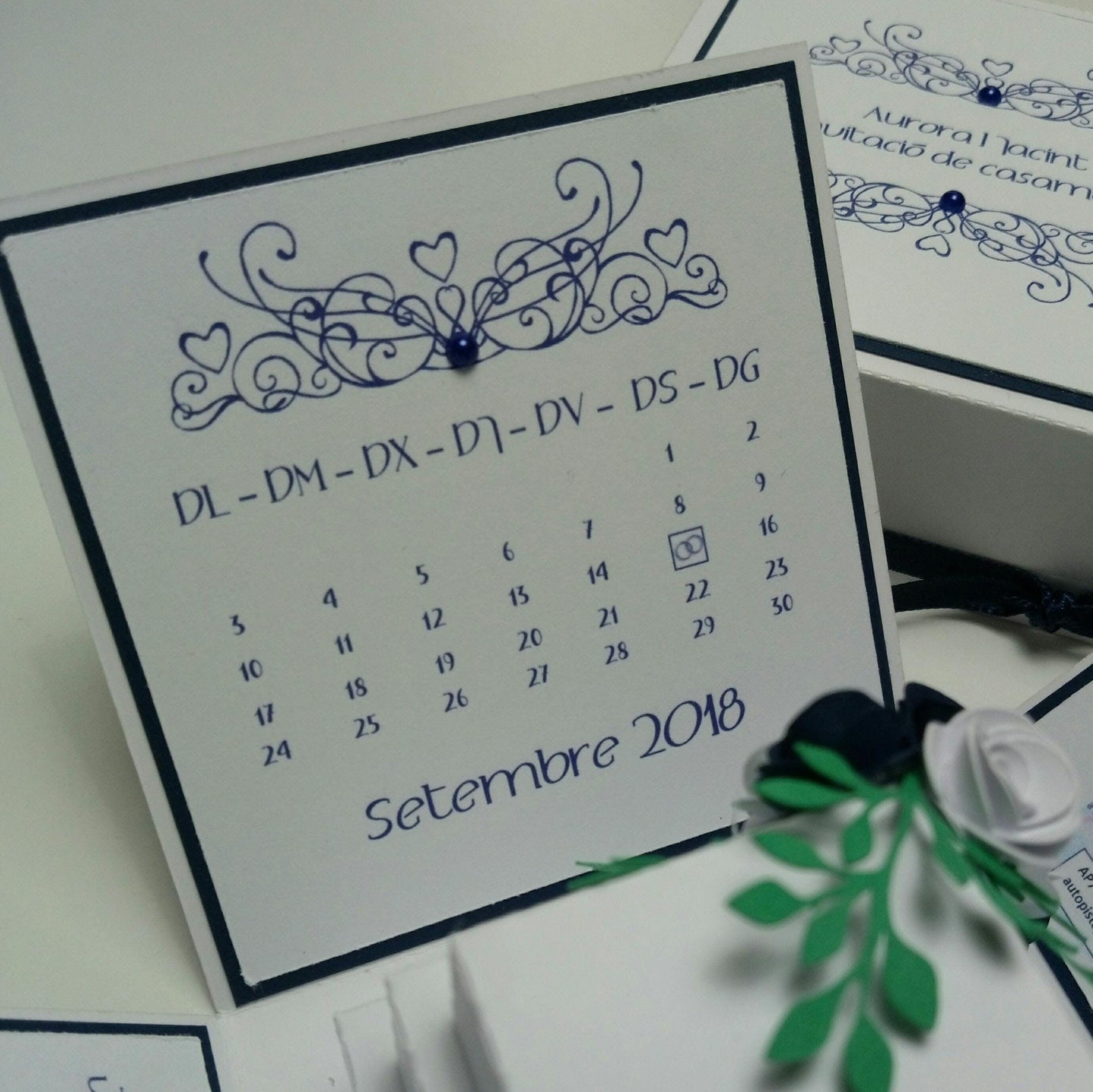 Exploding Wedding Invitation Box featuring a blue-themed calendar design with a decorative paper flower, personalized wedding details, and a central three-tier cake, showcasing luxury bespoke stationery.