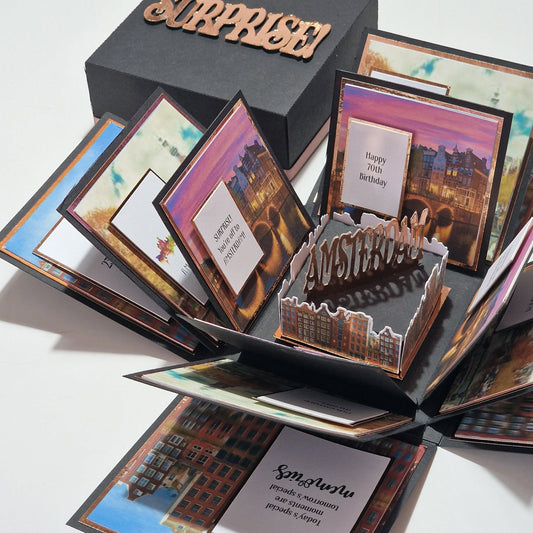 Exploding Occasions Box - Trip Reveal AMSTERDAM features a detailed pop-up design of Amsterdam's iconic canal houses, with paper panels and space for personalized details, perfect for a surprise trip announcement.