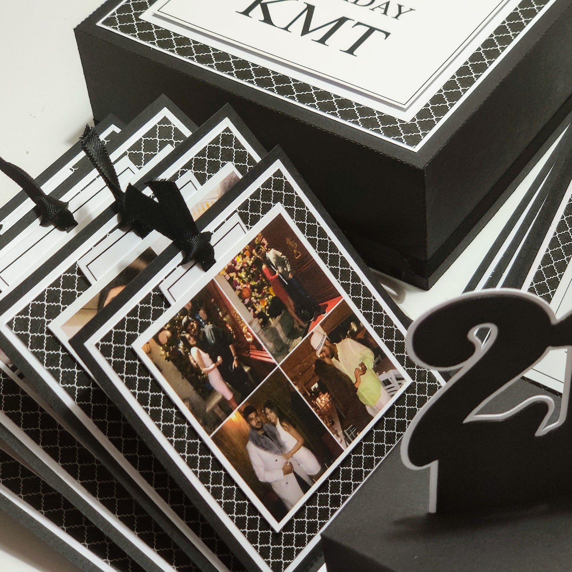 Exploding Memory Photo Box - Surprise Gift - Keepsake Album Box features a geometric black-and-white exterior. It opens into a cross-shaped display with layered compartments, ribbons, and a central space for mementoes.