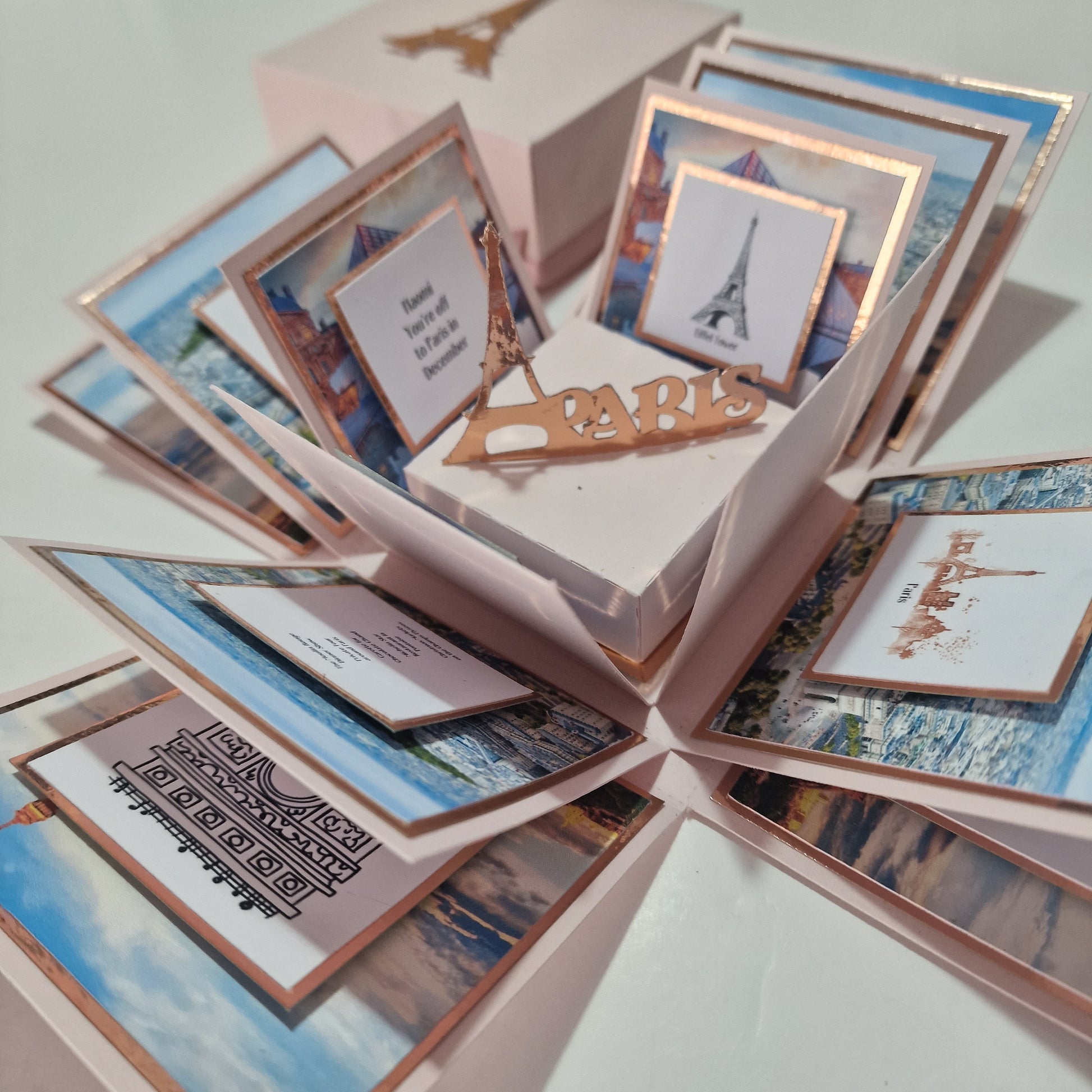 Paris - Special Occasion Celebration Trip Reveal Explosion Box showcasing a freestanding Eiffel Tower and paper panels detailing a Paris-themed surprise trip, with customizable elements for a personalized touch.