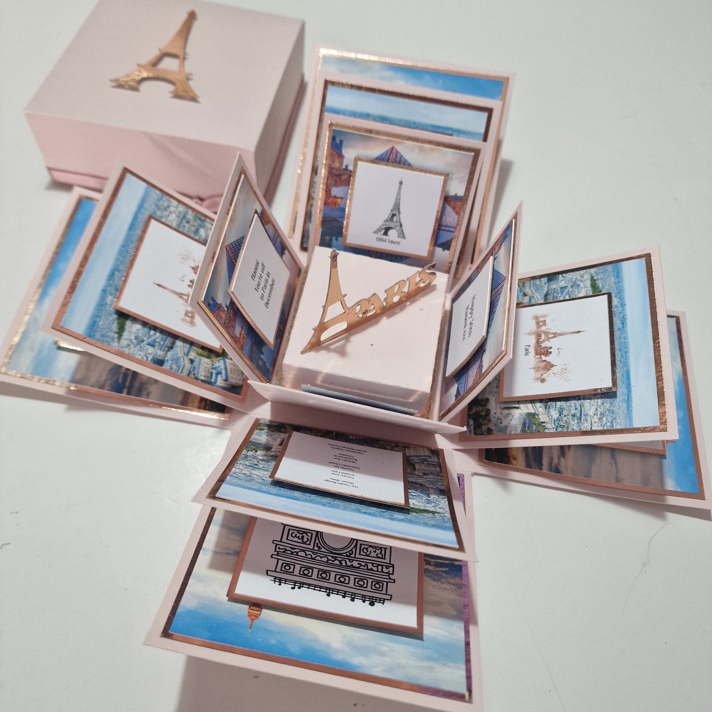 Paris - Special Occasion Celebration Trip Reveal Explosion Box featuring close-up elements: a book, tower image, and picture frame, meticulously crafted to unveil a surprise Paris trip with personalized details.