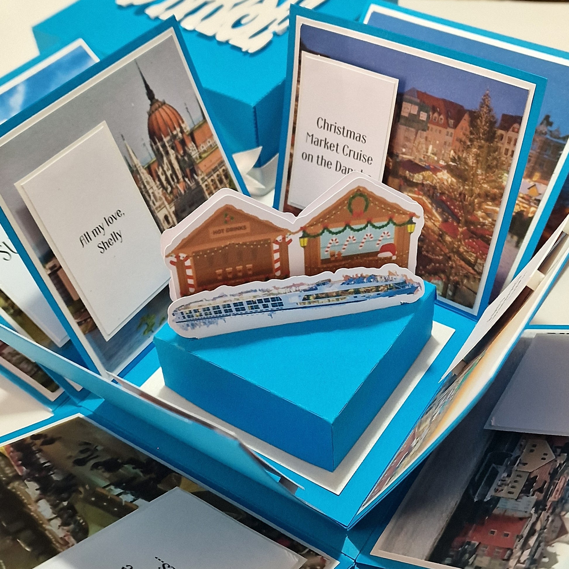Close-up of the Christmas Markets Exploding Trip Reveal Gift Box, featuring a detailed sticker and a white card with black text, designed to unveil holiday plans with festive charm.