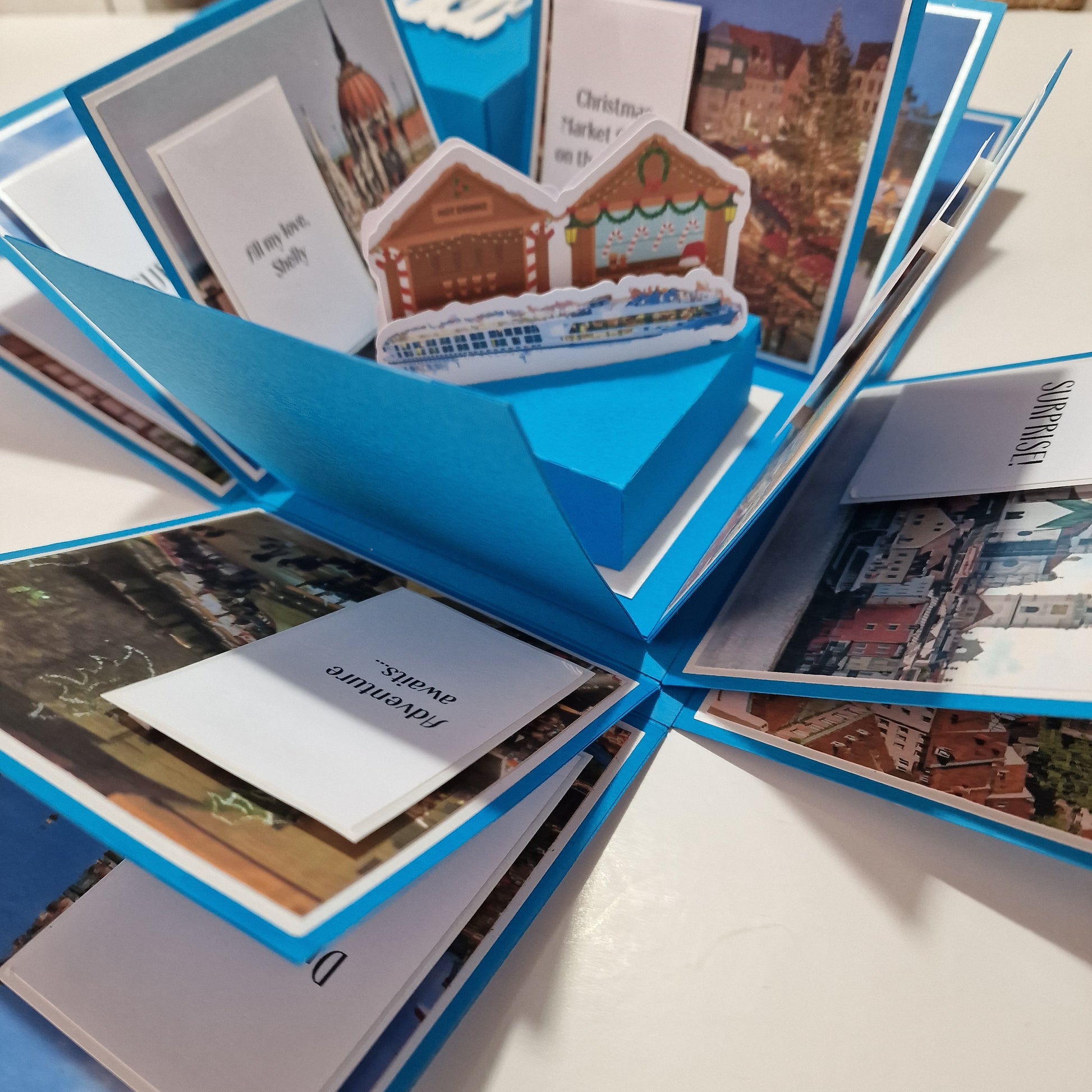 Close-up of the Christmas Markets Exploding Trip Reveal Gift Box, featuring a blue box with a festive design and personalized white paper insert, perfect for revealing holiday travel plans.