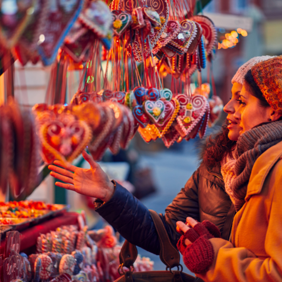 Two people at a market stall with gingerbread hearts and other treats.