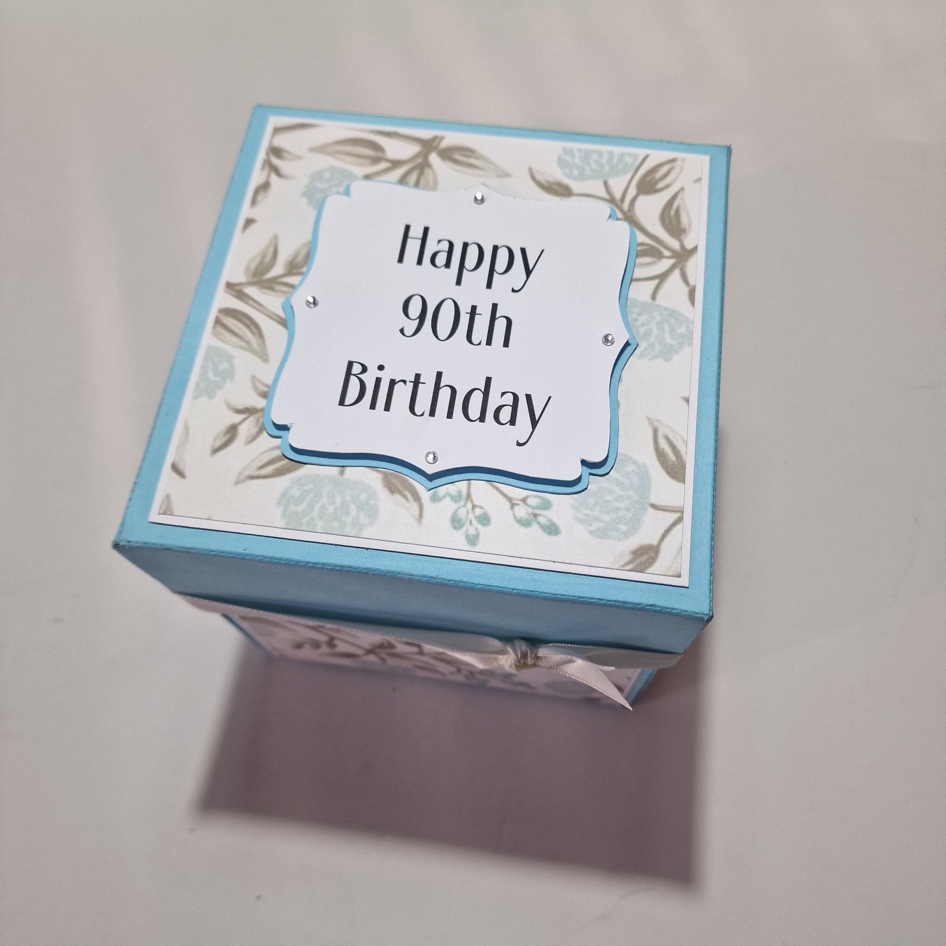Pastel Blue Florals Birthday Celebration Pop-Open Box Card featuring intricate floral patterns and designed to open up, revealing a festive surprise. Ideal for adding a special touch to birthday celebrations.