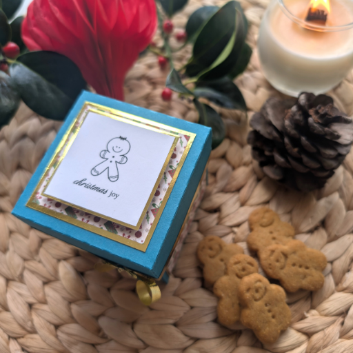 Exploding Christmas Box Card with Gingerbread Recipe – Handmade Festive Keepsake, Unique Holiday Gift Idea, wrapped in teal, featuring a gingerbread design and Christmas joy, surrounded by cookies, candle, pine cone, and festive greenery.