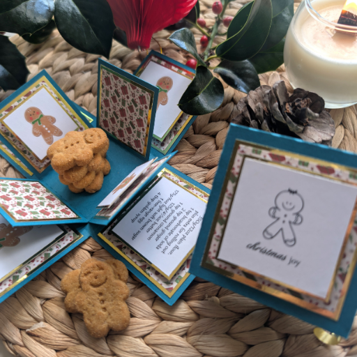 Exploding Christmas Box Card with Gingerbread Recipe – Handmade Festive Keepsake, Unique Holiday Gift Idea, displayed with gingerbread-man illustrations, real gingerbread cookies, holly leaves, pine cone, and lit candle.