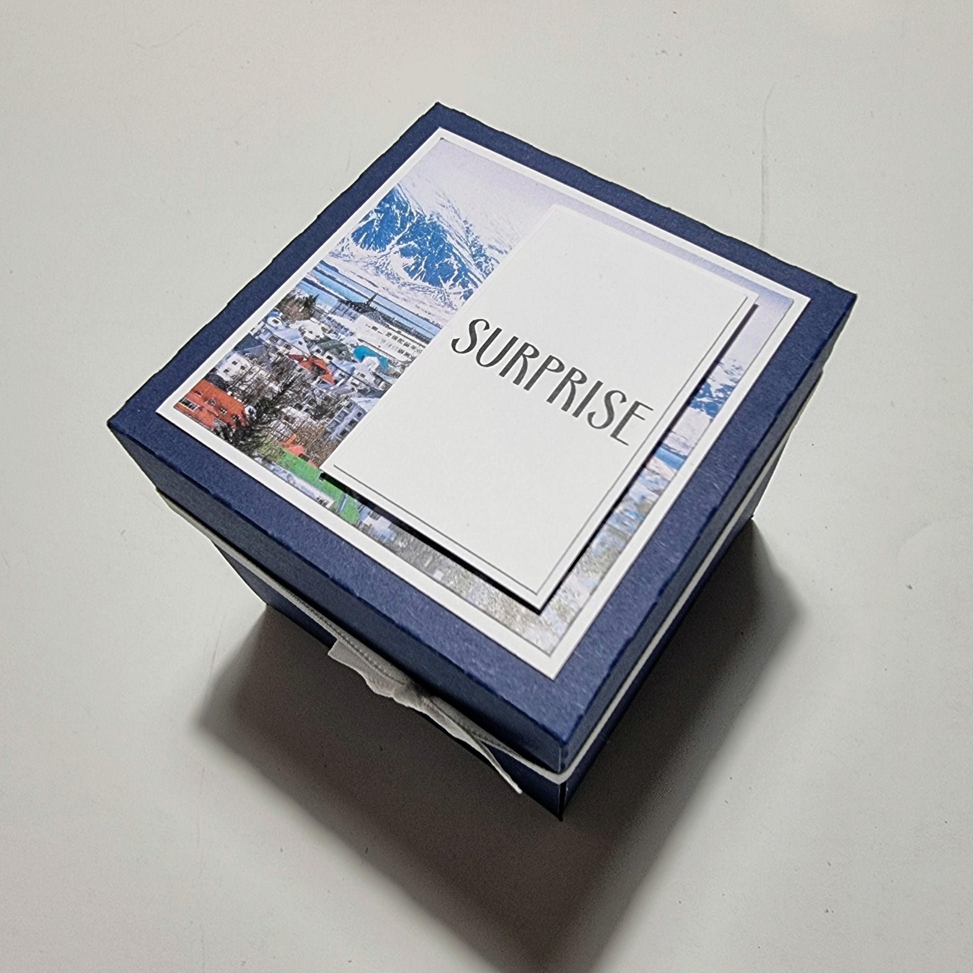 Exploding Occasions Box - Trip Reveal ICELAND, a decorative blue box with a white label, featuring surprise trip details for Iceland with landscape and verse panels, ideal for special celebrations.