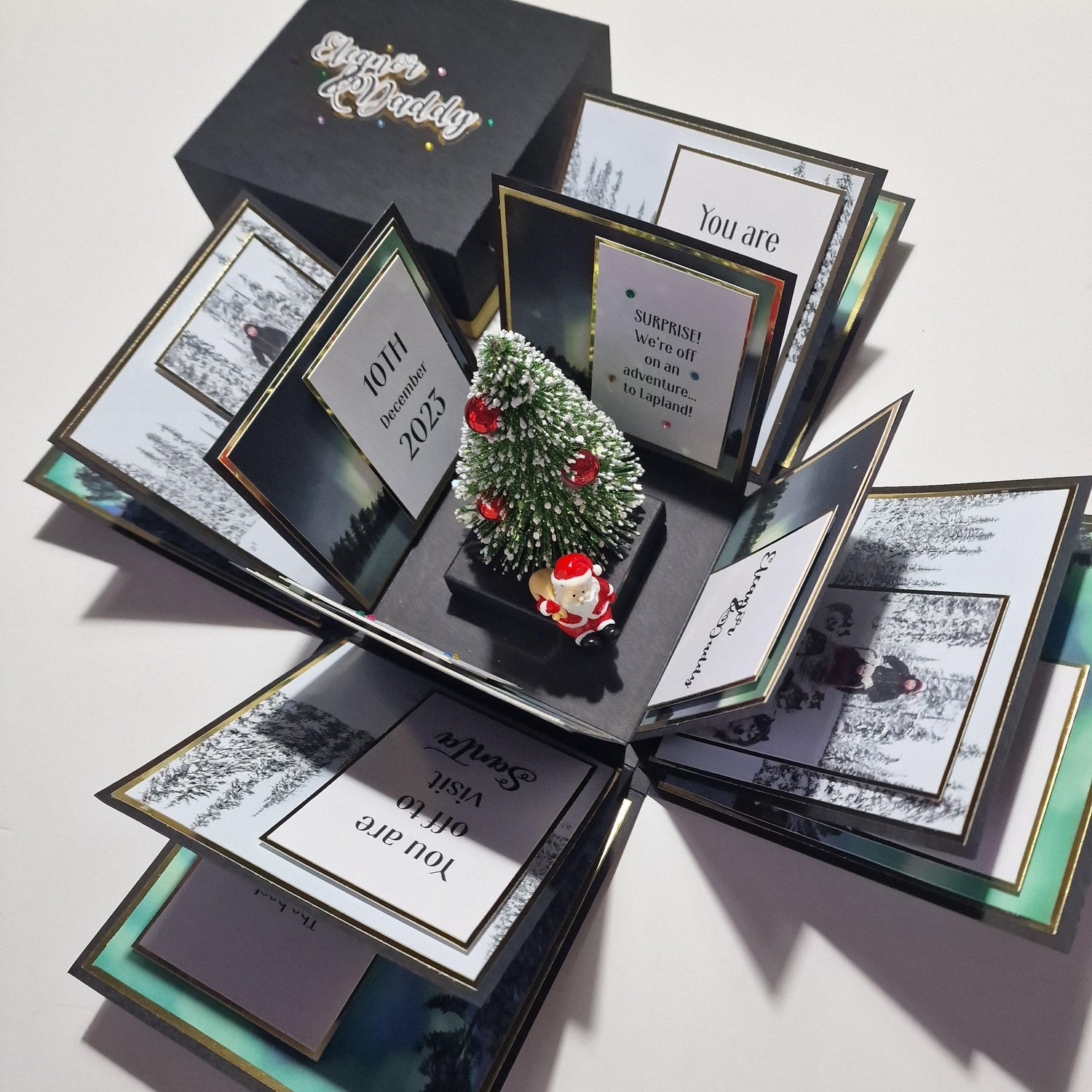 Lapland Christmas Trip Reveal box featuring a miniature Christmas tree with red ornaments, snow, and a Santa figurine, designed to unveil a surprise trip with personalized details.
