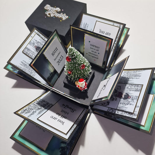 Lapland Christmas Trip Reveal box featuring a miniature Christmas tree with red ornaments, snow, and a Santa figurine, designed to unveil a surprise trip with personalized details.