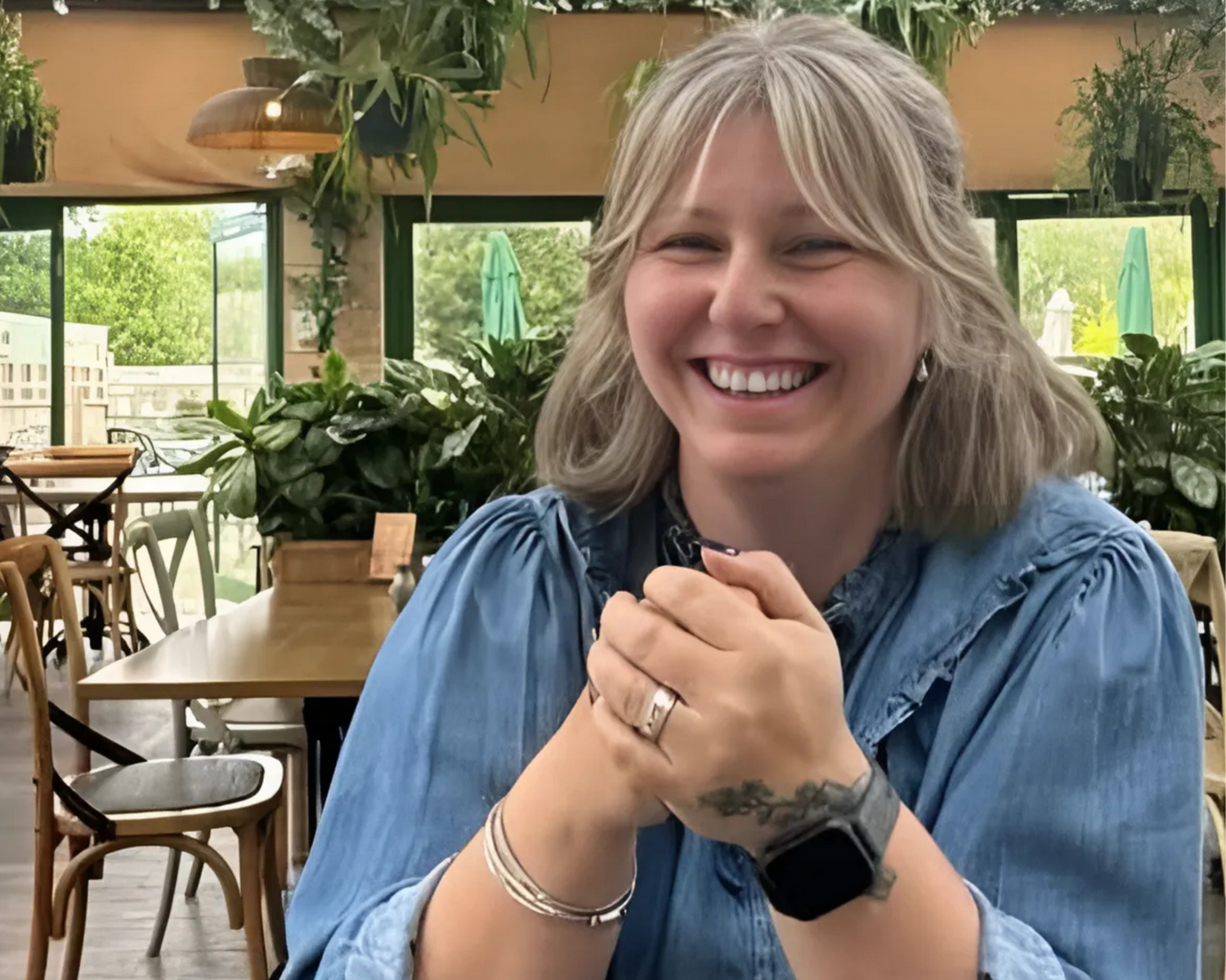 Woman sitting in a restaurant with plants and tables in the background