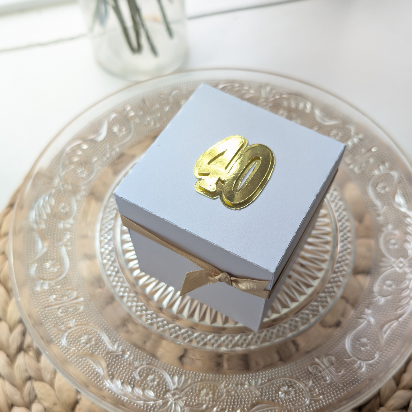 New York - Silver Grey Graffiti Styled - Surprise Special Occasion | Celebration Trip Reveal Explosion Box sits on a glass cake plate, wrapped in white paper with a gold ribbon and metallic “40” emblem.