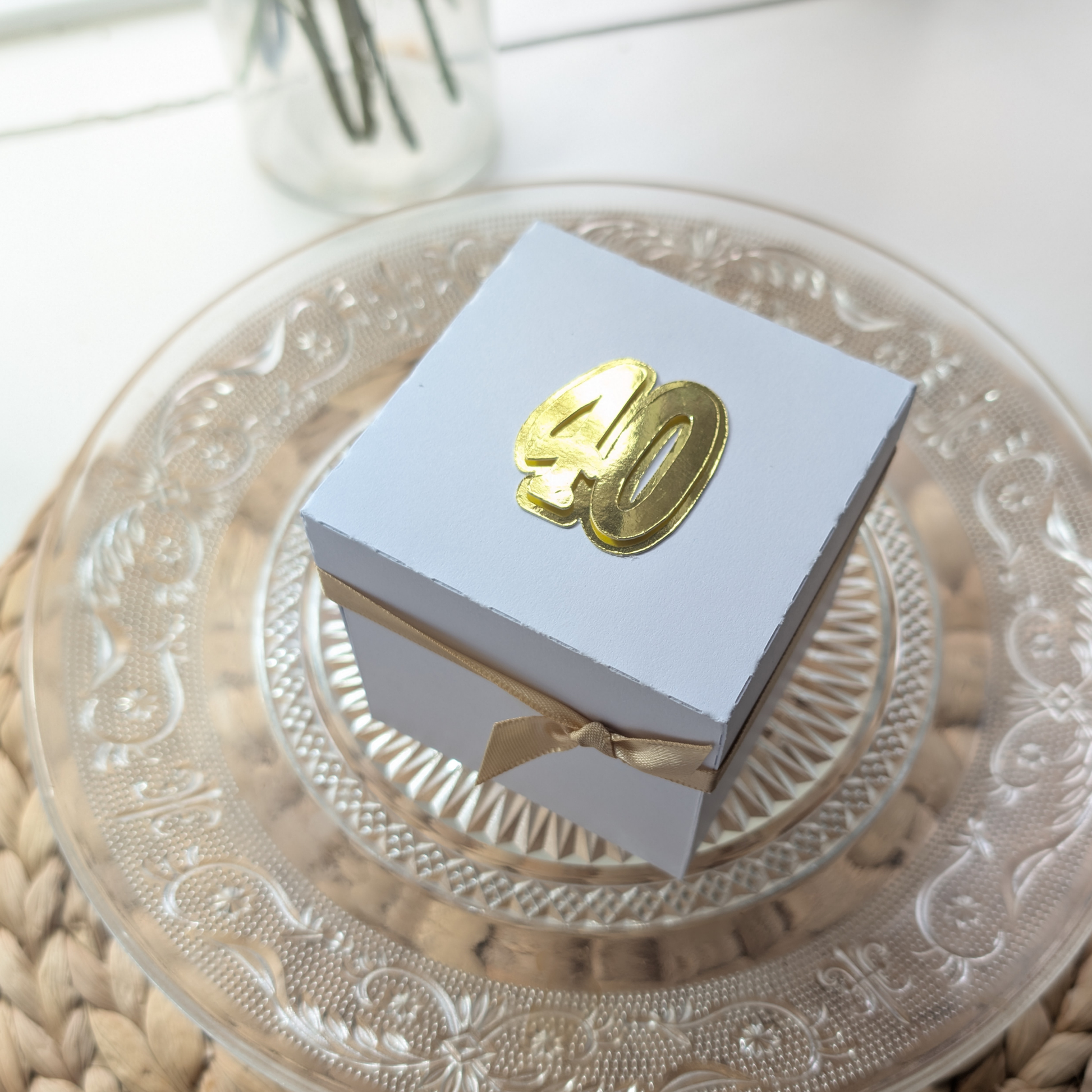 New York - Silver Grey Graffiti Styled - Surprise Special Occasion | Celebration Trip Reveal Explosion Box sits on a glass cake plate, wrapped in white paper with a gold ribbon and metallic “40” emblem.