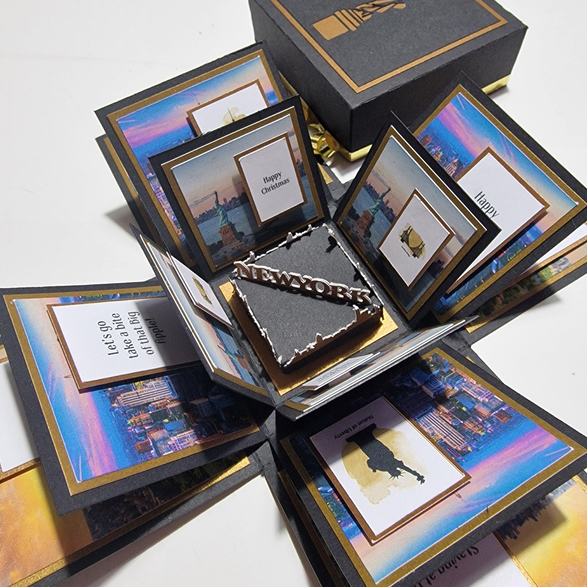 Exploding Occasions Box - Trip Reveal NEW YORK: A black box with gold trim, featuring New York-themed panels, a Statue of Liberty centerpiece, and space for personalized trip details and messages.