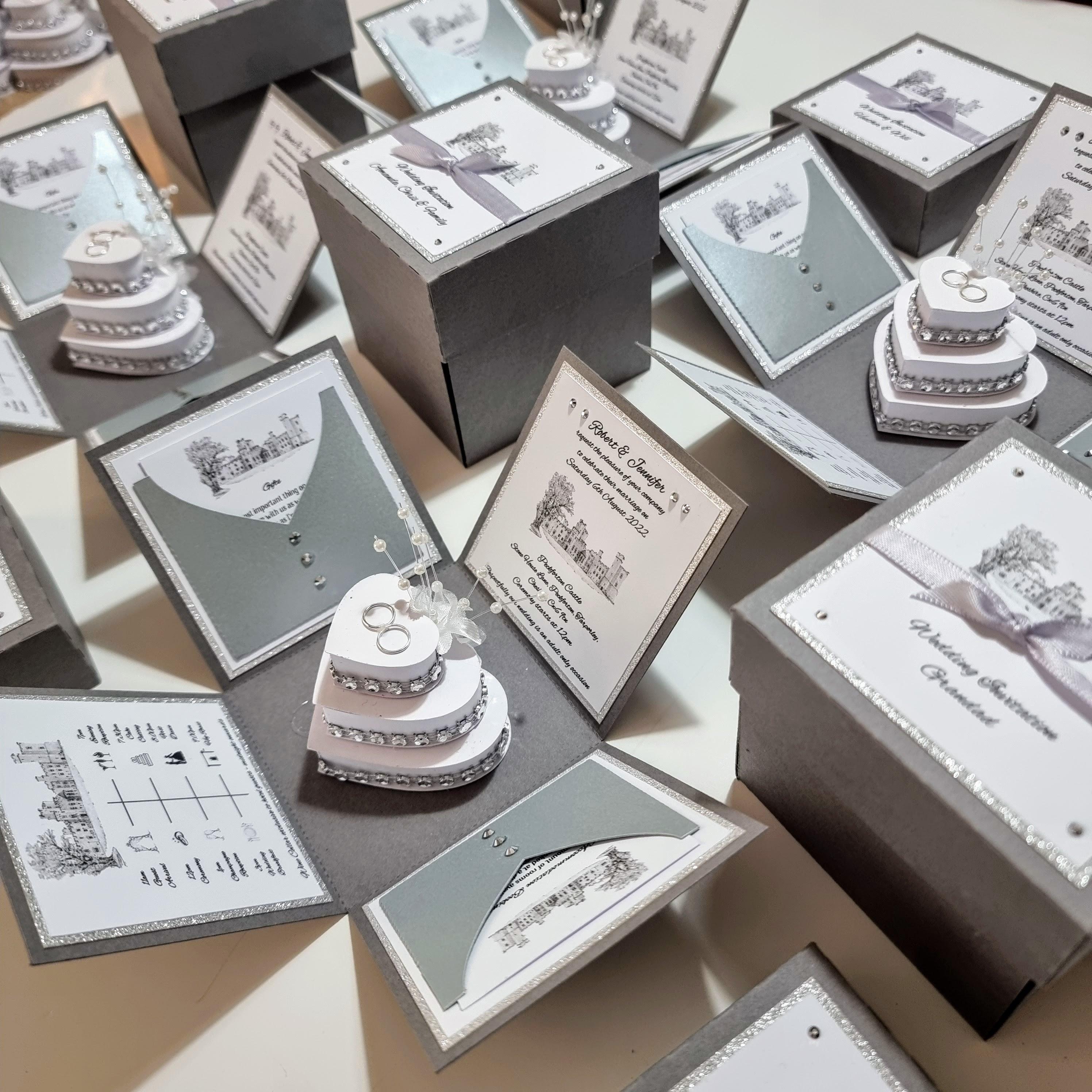 Illustrated Style Exploding Wedding Invitation Boxes featuring a unique square design, with panels for invitations and event details, and a heart-shaped cake centerpiece adorned with rings, perfect for luxury wedding stationery.