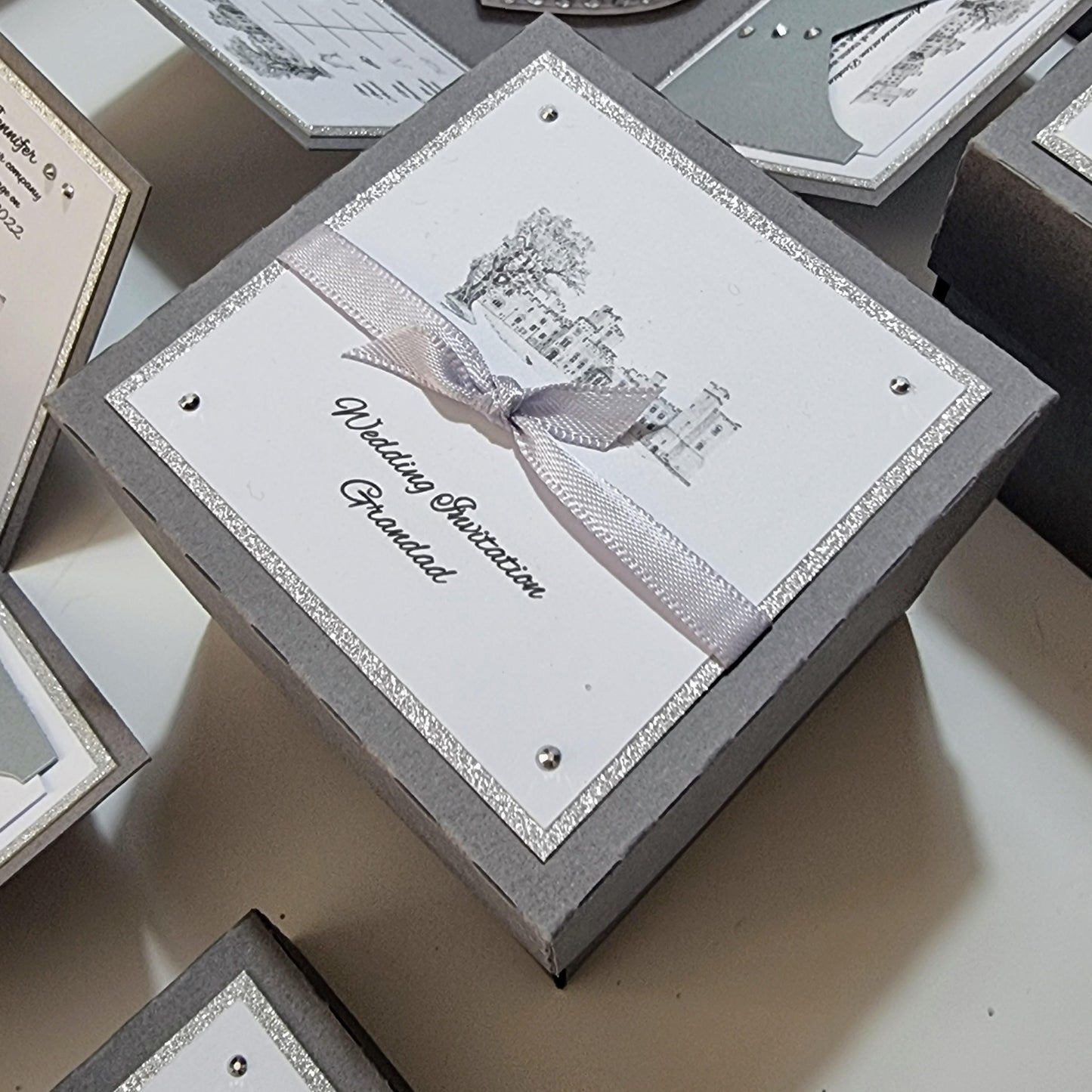 Illustrated Styled Exploding Wedding Invitation Boxes displaying intricate panels for invitation details, event timeline, and decorative elements like a heart-shaped cake with rings, embodying luxury and bespoke wedding stationery.
