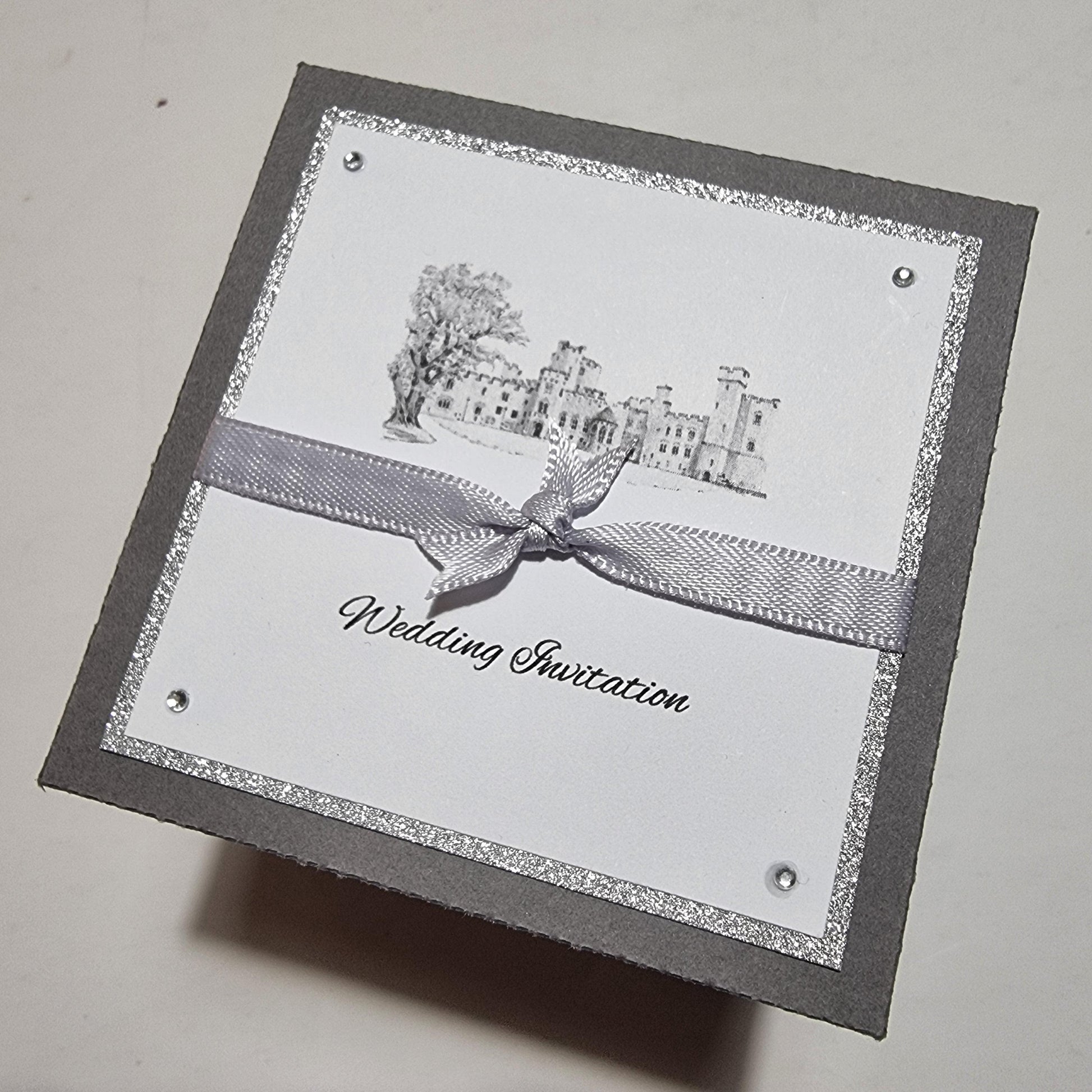 Illustrated Styled Exploding Wedding Invitation Boxes featuring a square card with a ribbon, showcasing detailed venue illustration and event timeline, perfect for bespoke wedding stationery and save-the-date announcements.