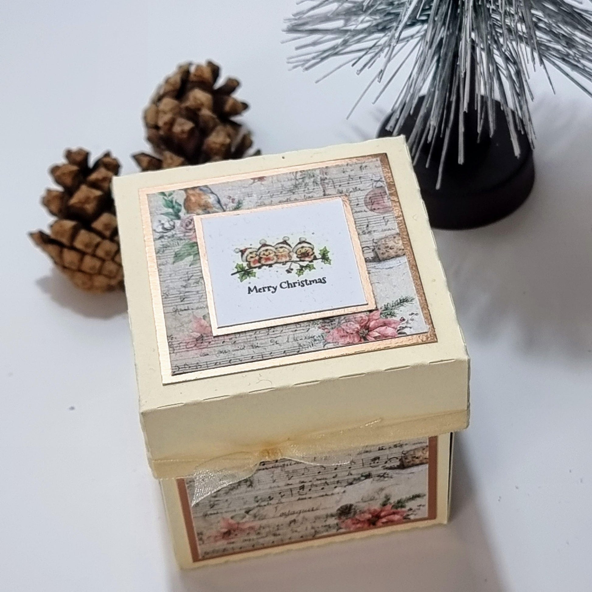 Rocking Robin Christmas Candle Box featuring a ribboned cream box with pine cones, a votive candleholder, and a card depicting festive robins.