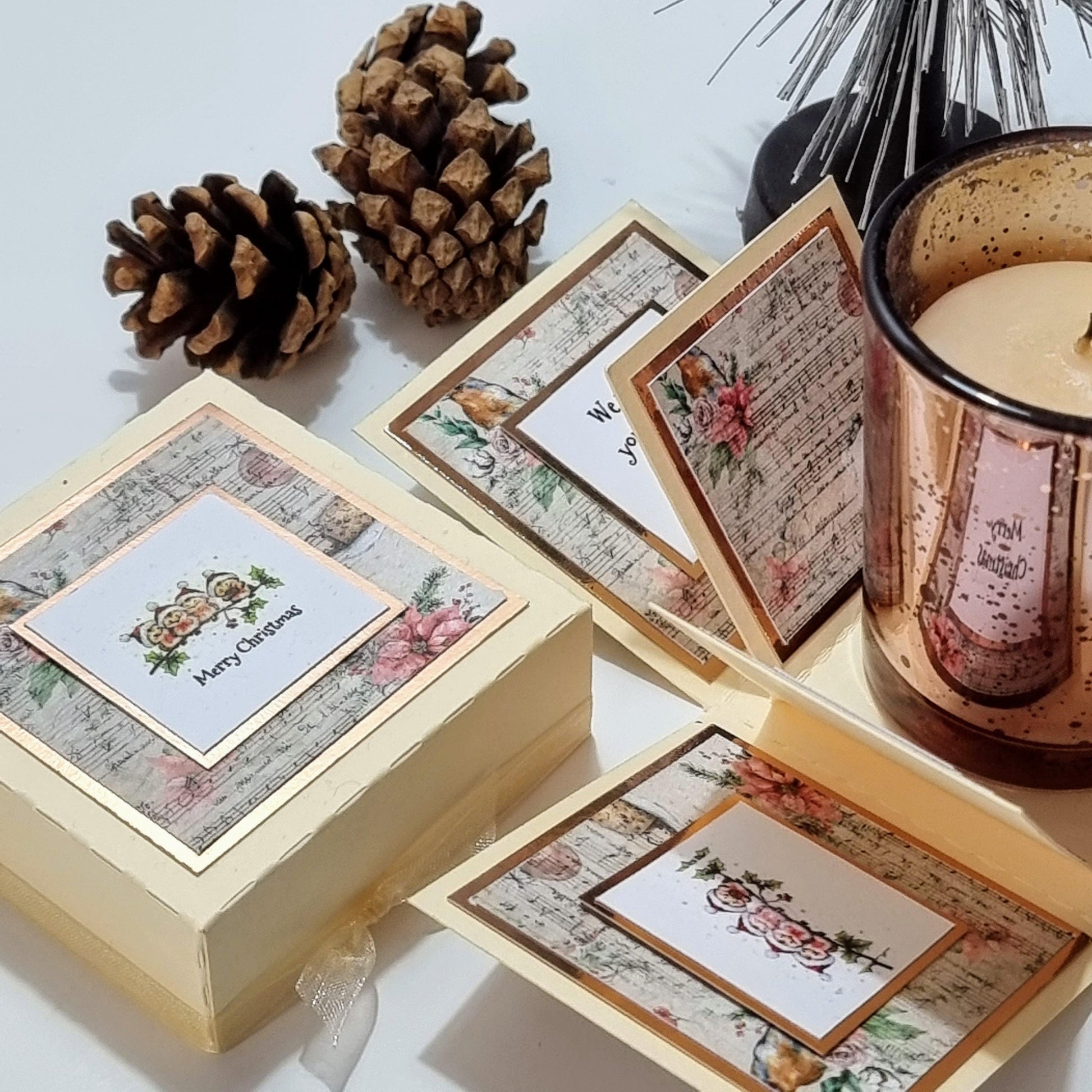 Rocking Robin Christmas Candle Box featuring a glass votive candleholder and a square box with Christmas Robins, accompanied by a festive-scented candle in a decorative clotted cream and rose gold design.