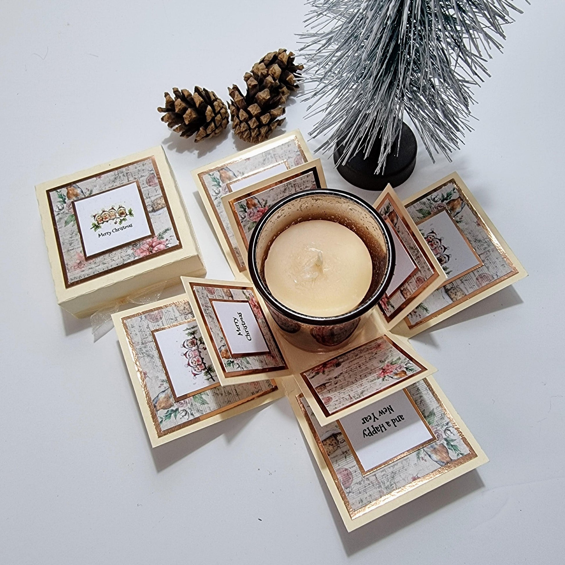 Rocking Robin Christmas Candle Box featuring a glass votive candleholder with pine cones and a small tree, accompanied by a festive greeting card in a clotted cream square box.