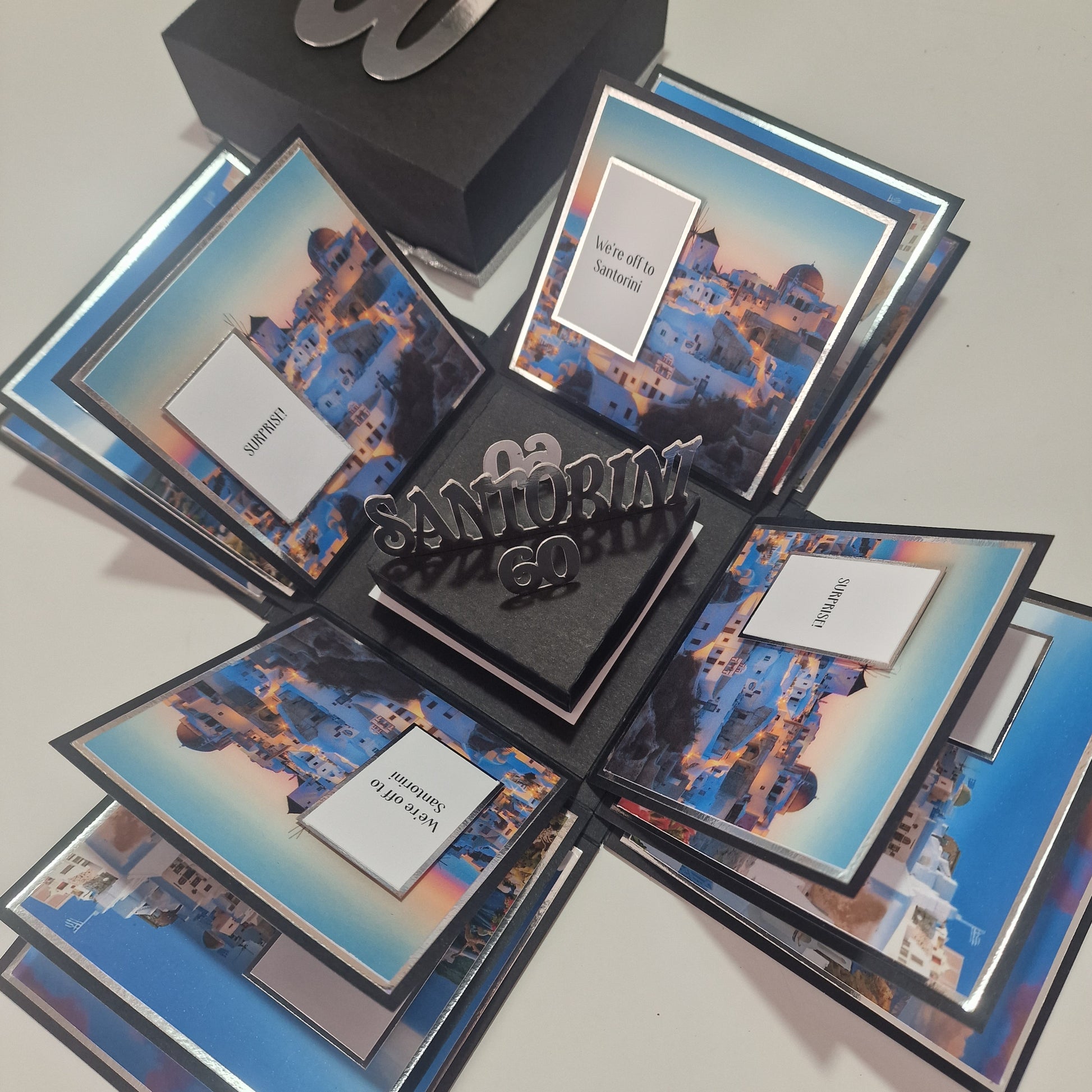 Santorini Exploding Trip Reveal Box – Unique Holiday Surprise Gift: A pop-up box with Santorini-themed photos, unfolding panels, and a central Santorini 60 insert, announcing a memorable 60th-birthday trip.