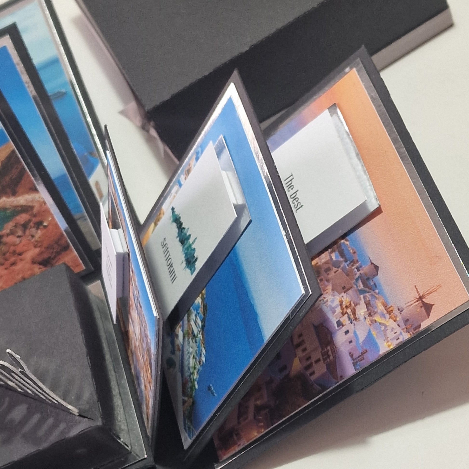 Santorini Exploding Trip Reveal Box: A hand-made accordion-style album with vivid Santorini photos unfolds in zig-zag fashion, revealing surprise elements and the ultimate trip announcement to Santorini.