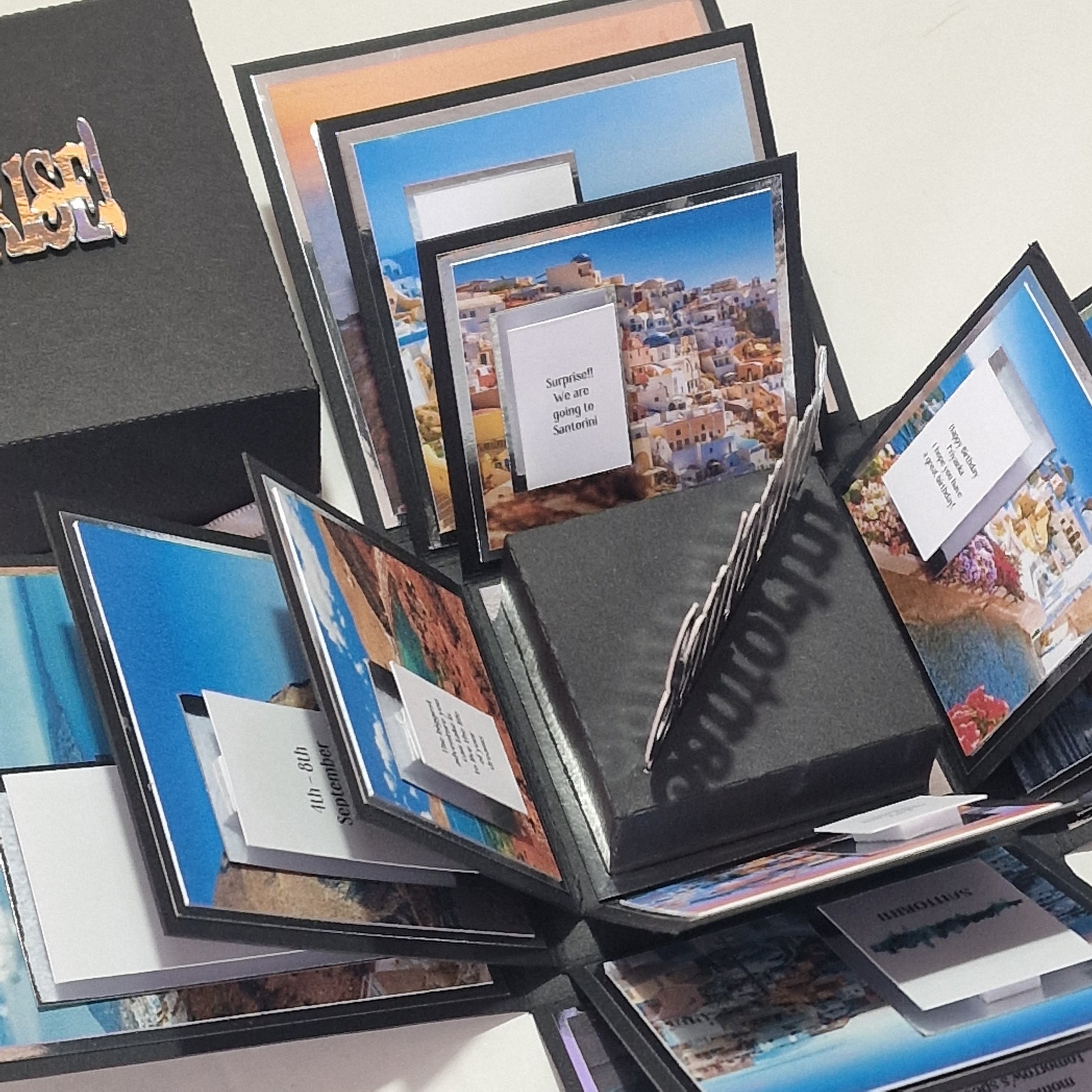 Santorini Exploding Trip Reveal Box: A handcrafted gift that unfolds layers with Santorini photos and pop-out cards, culminating in a surprise trip announcement to the Greek island.