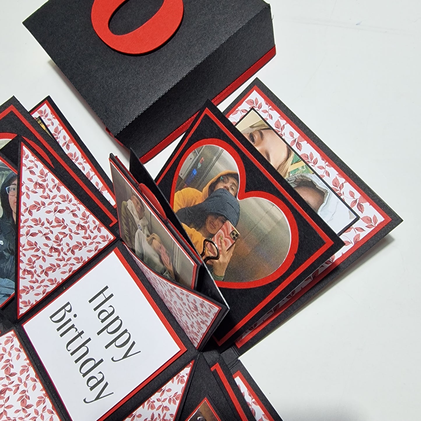 Exploding Memory Photo Box - Black & Red Leaves: A sleek black box with red leaf embellishments, unfolds to reveal photo panels and compartments for keepsakes, ideal for cherished memories and gifts.