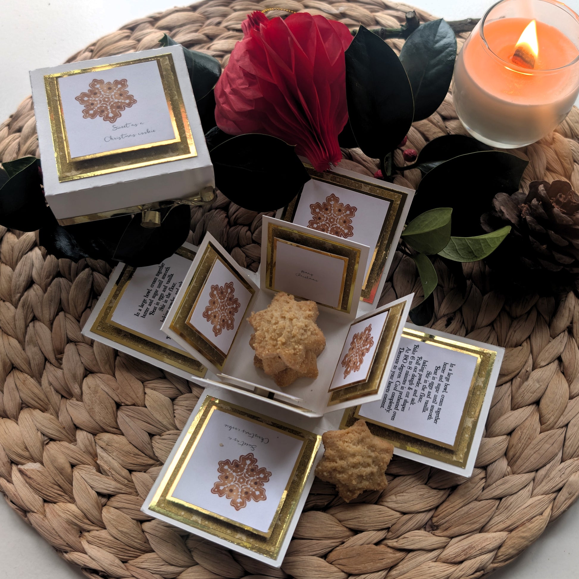 Exploding Christmas Box Card with Shortbread Recipe – Handmade Festive Keepsake featuring a white box with gold trim, star-shaped cookies, holiday cards, greenery, a red ornament, pine cone, and lit candle.