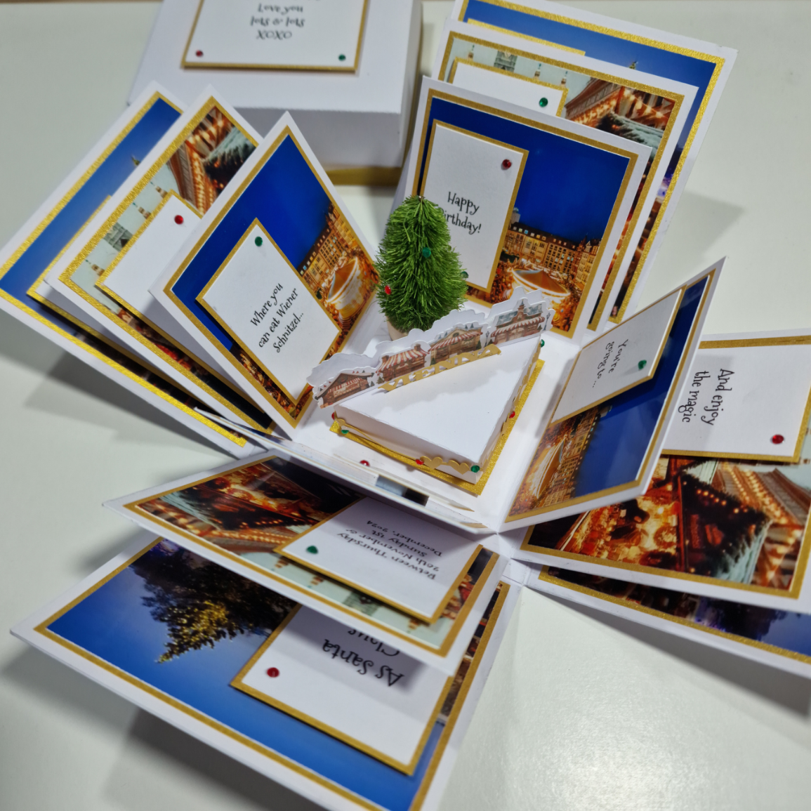 Close-up of the Christmas Markets Exploding Trip Reveal Gift Box, featuring a white card with black text and a red gem, highlighting a unique holiday tradition surprise.
