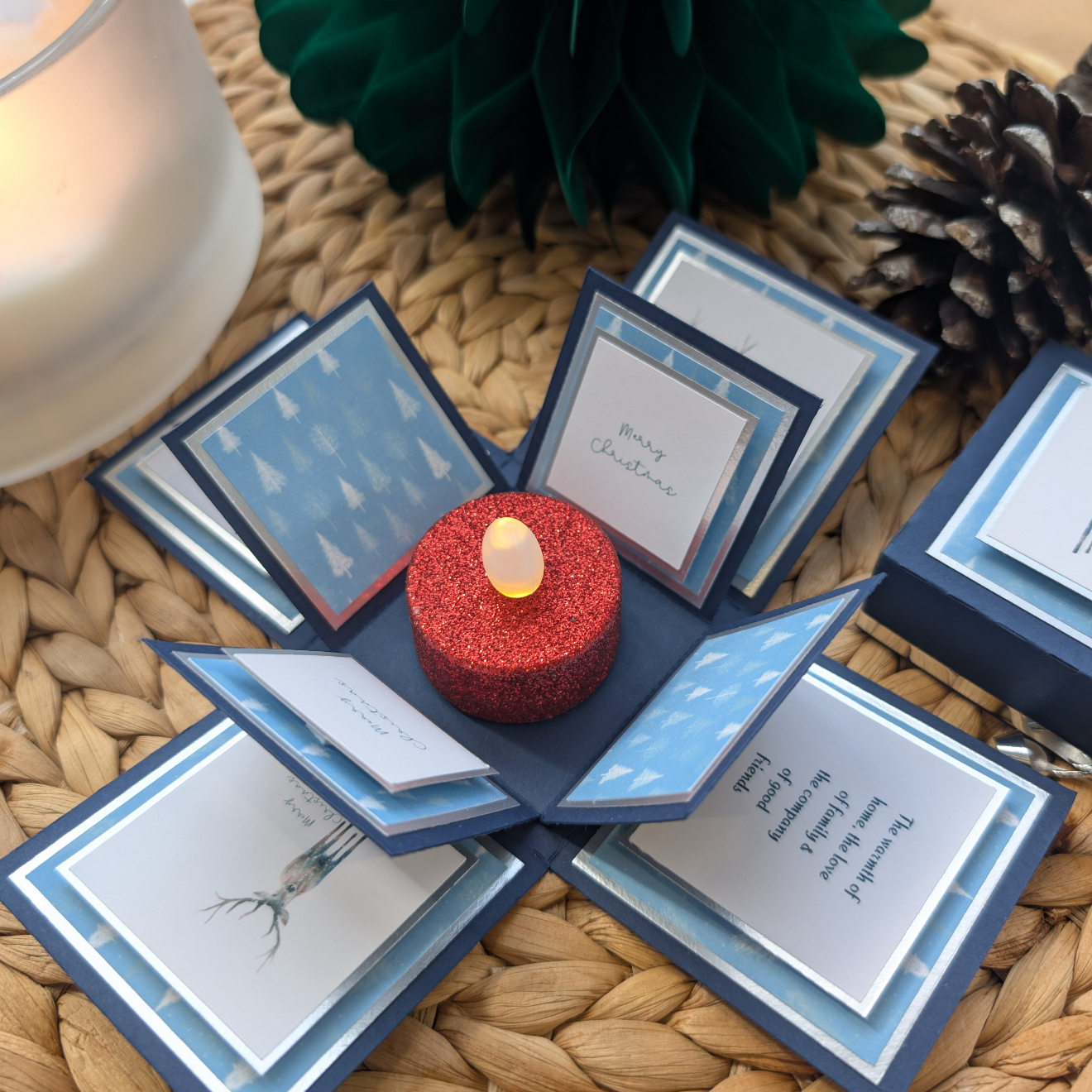 Winter Stagg Christmas Box Card featuring a pop-up design with a central LED tealight, surrounded by festive stag sketches, Merry Christmas text, and snowy tree patterns on layered fold-out panels.