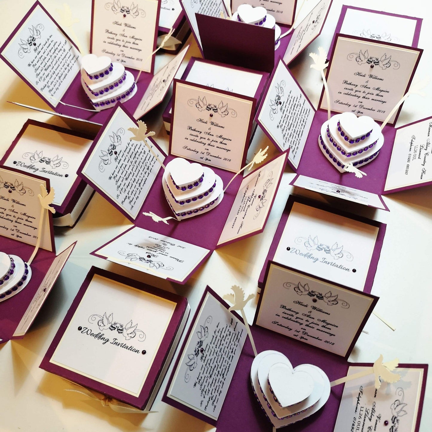 Hearts & Doves Range - In Purple & Cream.   A totally unique 3'' Square Exploding Wedding Invitation Box featuring two fixed panels, One with Invitation details and the other with Venue details. There are also two waistcoat-styled pockets with pull-out panels containing Menu &amp; Menu Choices Cards plus RSVP Card &amp; Gift Poem. The centre of these boxes contains a three-tier Heart-shaped Wedding cake decorated with diamonds and color-coordinating ribbon strips. 