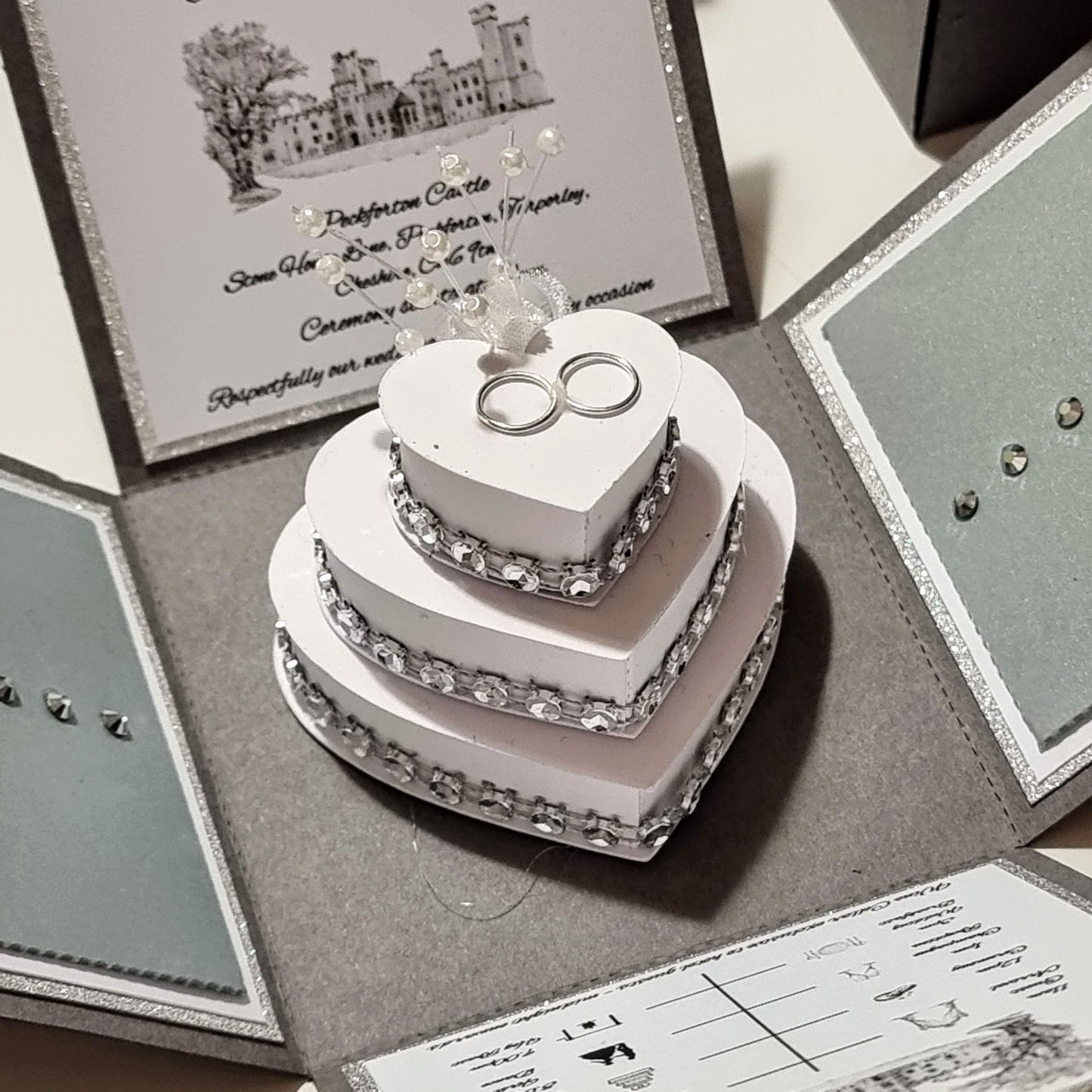 Wedding cake decorated with diamonds, colour-coordinated flowers &; a pair of wedding rings.