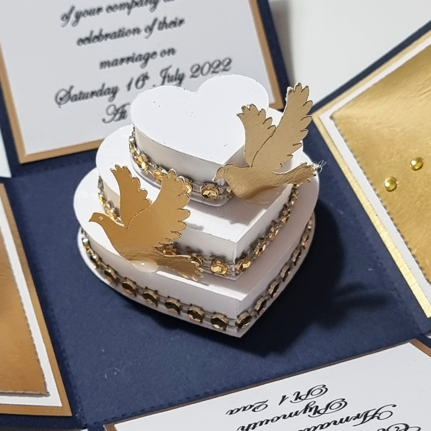Hearts & Doves Range in Classic Navy Blue and Gold. Unique 3'' Square Exploding Wedding Invitation Box featuring two fixed panels, One with Invitation details and the other with Venue details. Gold Doves sit on the three tier cake.